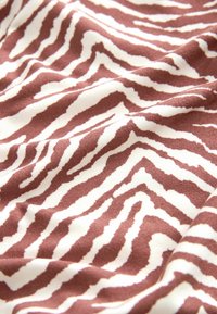 Brun og hvidt stof med et bølget zebra-stribemønster, der har en blød tekstur og en let glans, foldet for at vise dybde og detaljer.