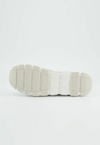 Bílá gumová podrážka boty s texturovaným gripem, obsahující horizontální drážky a zaoblenou špičku. Čisté logo značky na boku.