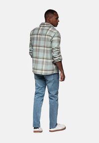 Camisa de cuadros en tonos verde claro y gris, hecha de una tela suave, con un corte relajado y cierre de botones, combinada con jeans azul claro.