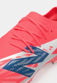 Kirkas korallinvärinen kenkä, jossa on teksturoitu päällinen, korallinväriset nauhat ja suuri sininen ja hopeinen zigzag-kuvio sivussa.