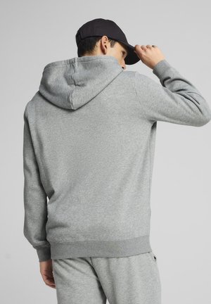 Grå sweatshirt med hætte, lange ærmer og ribbede manchetter. Blød tekstur, afslappet pasform. Båret med matchende grå bukser og en sort kasket.