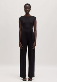 Schwarzer gerippter Jumpsuit mit kurzen Ärmeln, tailliertem Oberteil, weit geschnittenen Hosenbeinen und gebundenem Taillendetail, gefertigt aus weichem, dehnbarem Material.