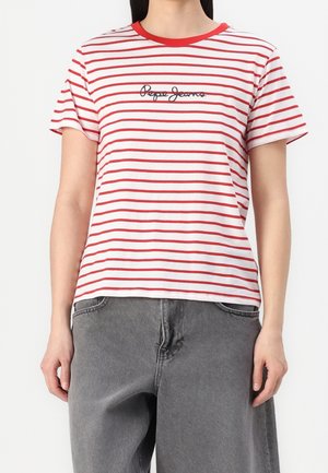 Kobieta nosząca biało-czerwoną pasiastą koszulkę z krótkim rękawem z napisem „Pepe Jeans”, zestawioną z luźnymi szarymi dżinsami.