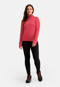 Roze langmouw zip-up top met duimgaten, gecombineerd met zwarte legging en stevige zwarte wandelschoenen met rode details.