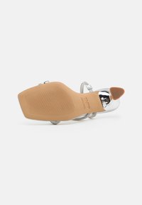 Sølv sandaler med stropper, spiss tå, teksturert beige såle og metalliske detaljer. Har gummigrep og dekorative stropper.