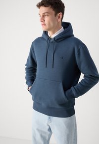 Marineblauer Hoodie mit Kordelzügen, Kängurutasche und besticktem Logo. Hergestellt aus weichem Stoff mit glatter Textur. Lässiger Schnitt.