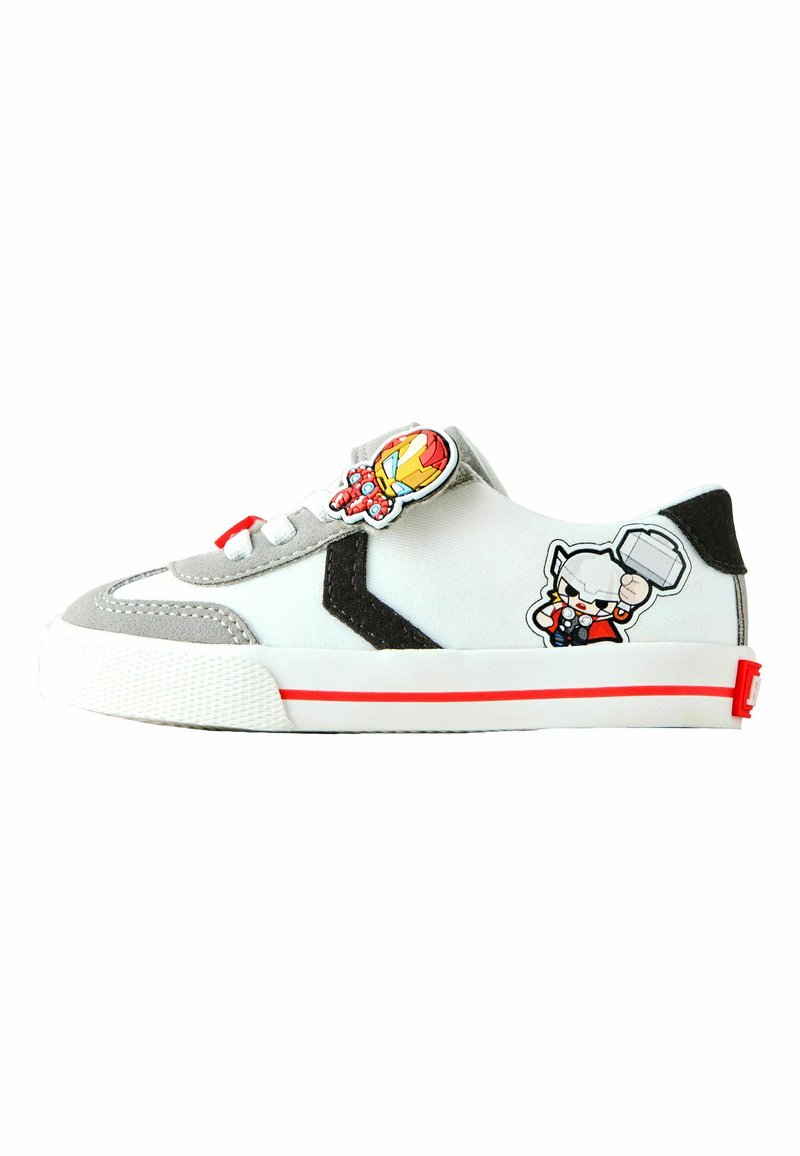 Zapatillas deportivas con parte superior de lona blanca, detalles grises, logotipo negro y franja roja en la suela. Presentan parches de dibujos animados de personajes en la lengüeta y los laterales.
