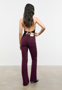 Bordo široke traperice s srednjim strukom, stražnjim džepovima i crni halter top s vezanjem na stražnjoj strani.