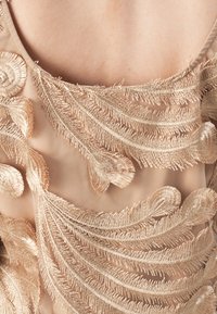 Nakedstoff mit filigraner, gestaffelter goldener Stickerei, die wirbelnde Blattmuster und strukturierte Akzente zeigt. Nahaufnahme des Kleidungsdetails.