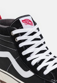 Mustad musta kõrge säärega sneakers valgetest paeltest, valgetest külgtriipudest ja punasest logost keelel. Materjal on kanvase ja nubuki aktsentidega.