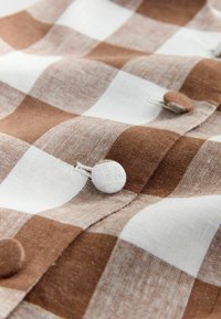 Primo piano di tessuto a quadretti marroni e bianchi con bottoni ricoperti dello stesso tessuto cuciti sul materiale.