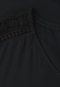 Gros plan sur un tissu noir avec une bordure en dentelle florale et un détail de couture en diagonale.