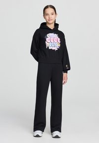 Felpa nera corta con una stampa grafica colorata, abbinata a pantaloni neri a gamba larga e sneakers bianche. Tessuto liscio con una vestibilità comoda.