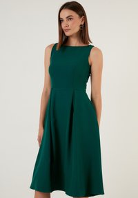 Rochie verde fără mâneci, cu o siluetă fit-and-flare, care prezintă un decolteu rotund, fustă plisată și textură de stofă netedă.