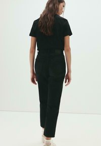 Schwarzes Baumwoll-T-Shirt kombiniert mit hochgeschnittenen schwarzen Jeans. Das Shirt hat einen Rundhalsausschnitt, und die Jeans haben eine schmal zulaufende Passform sowie Gesäßtaschen.