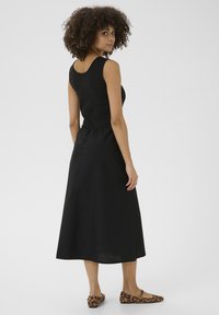 Svart ärmlös klänning med en åtsittande bodice och en svävande kjol i midilängd. Tyget ser slätt ut, i kombination med platta skor med leopardmönster.