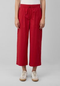 Pantaloni rossi a croppato con vita elastica e cordino. Realizzati in un tessuto leggero con una superficie liscia. Abbinati a sneakers bianche.