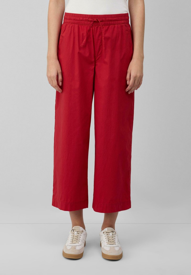 Pantaloni rossi a croppato con vita elastica e cordino. Realizzati in un tessuto leggero con una superficie liscia. Abbinati a sneakers bianche.