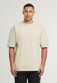 Beige Baumwoll-T-Shirt mit kurzen Ärmeln, Rundhalsausschnitt und lockerer Passform, mit glatter Textur und minimalistischem Design.