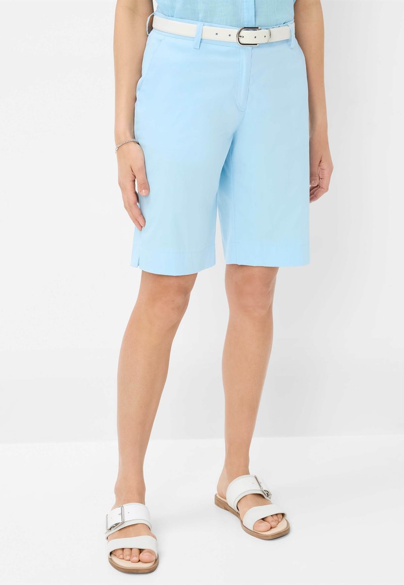 Shorts azzurri chiari con una texture liscia, lunga fino al ginocchio, caratterizzati da spacchi laterali. Abbinati a sandali bianchi con dettaglio a cinturino e fibbia.