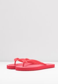 Bright pink flip-flops made of smooth rubber, featuring a two-strapped design and a textured footbed, with a wave-patterned sole edge.