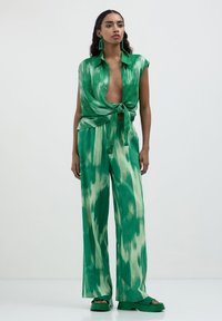 Grünes Batik-Outfit mit einem kurz geschnittenen, offenen Hemd mit kurzen Ärmeln und weit geschnittenen Hosen, beide aus leichtem Stoff.