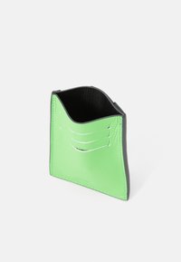 Grøn læderkortholder med sorte kanter, der har fire kortpladser og et buet topdesign. Glat tekstur med syede detaljer.
