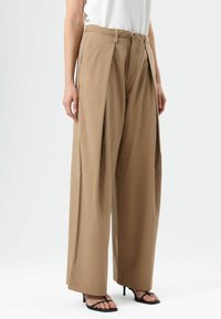 Beige wide-leg trousers with a belted waist, featuring soft fabric and front pleats. The model wears black strappy sandals.