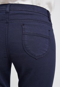 Marinblå jeans med en mjuk textur, med en bakficka med rundad form och subtila sömdetaljer vid kanterna.