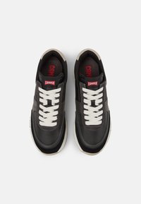 Czarne skórzane sneakersy z białymi sznurówkami i teksturowaną podeszwą środkową, z czerwonym logo "CAMPER" na języku i boku.