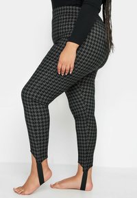 Leggings de pata de gallo en negro y gris con cintura alta y recortes en los tobillos. La tela es suave, proporcionando una silueta ajustada.