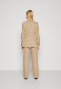 Beige sakový blejzer so štruktúrovanými ramenami a peplum dizajnom, kombinovaný s nohavicami so širokým strihom z rovnakého materiálu. Hladká textura.