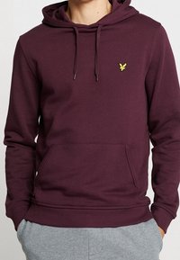 Sudadera burdeos de mezcla de algodón, con un bolsillo frontal, capucha con cordón y un pequeño logo amarillo en el lado izquierdo del pecho.