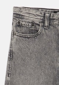 Γκρι τζιν denim με κλασικό σχεδιασμό πέντε τσεπών, με distressed λεπτομέρειες και μαύρα μεταλλικά στοιχεία στο μπροστινό μέρος.