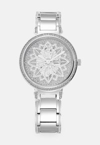Sølvklokke med en blomsterdekorert urskive, utsmykket med krystaller, og et polert metalarmbånd med lenker og dekorative detaljer.