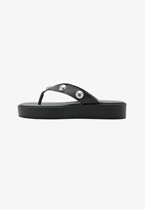 Sandale tongs plateforme noire avec une large bride ornée de trois gros clous argentés, semelle plate et entre-doigt, sur fond blanc.