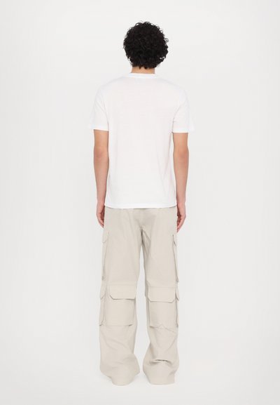 Tricou alb cu guler rotund și pantaloni cargo gri deschis cu mai multe buzunare. Outfittul are o croială lejeră și o textură netedă din bumbac.