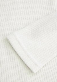 Biała, prążkowana tkanina o miękkiej fakturze, z zagiętym mankietem na jednym brzegu. Delikatne, błyszczące akcenty wszyte w całość.