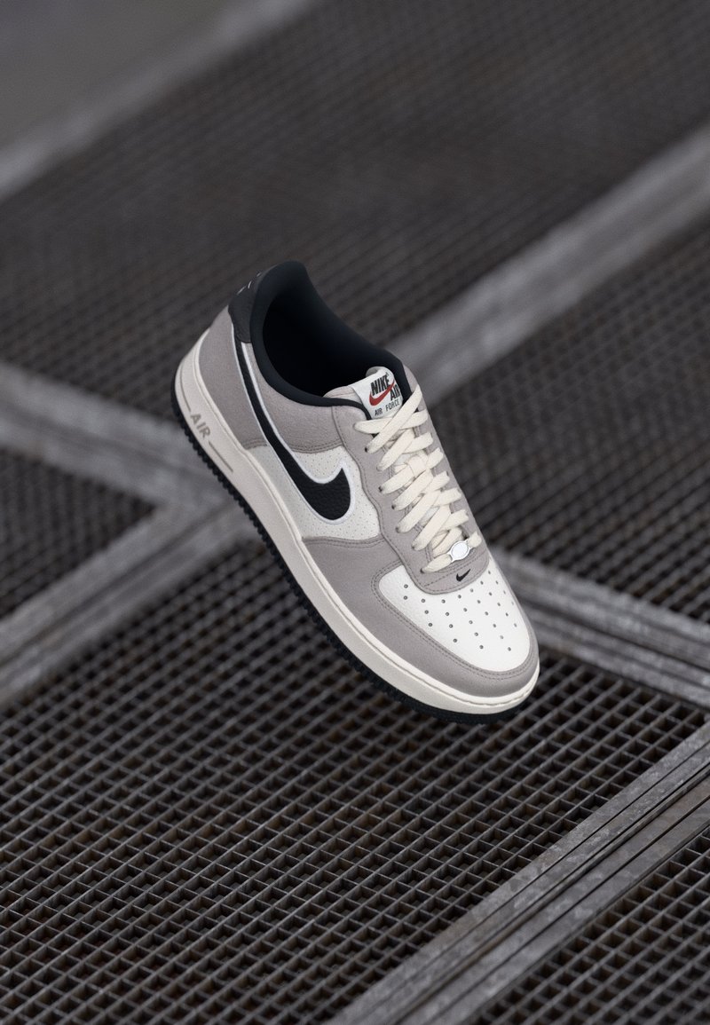 Nike Air Force 1 sneaker szürke és fehér színben, velúr és bőr felsőrésszel, lapos cipőfűzőkkel, perforált orr résszel és gumitalppal.