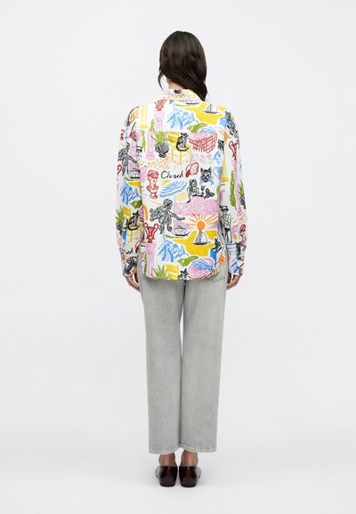 Chemise à col avec un motif graphique multicolore comprenant des chats, des plantes et des personnages. Associée à un pantalon large gris clair et des chaussures marron.