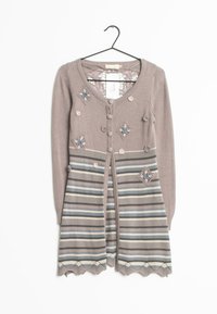 Beige cardigan med blommönsterbroderi, randig kjol, fem knappar och virkad dekoration. Har långa ärmar och dekorativ nederkant.