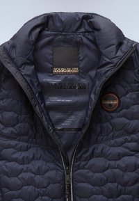 Navyblå quiltad jacka med foder och dragkedja. Innehåller en logotillbehör och skötselråd. Materialet är slätt och lätt polyester.