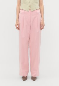 Różowe spodnie o szerokich nogawkach z plisami z przodu, wykonane z lekkiego materiału, mają czysty dół. Noszone z jasnym kamizelką.