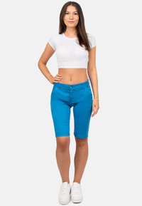 Bermuda shorts in denim blu con chiusura a bottone, dotati di tasche frontali e una texture liscia. Abbinati a una t-shirt corta bianca e sneakers bianche.