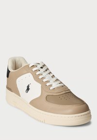 Beige lädersneakers med vita accenter, perforerat tåfack och kontrasterande svart häl. Har vita snörning och en liten logodetalj.