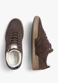 Bruna mockaskor med rund tå, bruna snörningar och beige gummisulk; har en logotyp på plösen och vit foder.