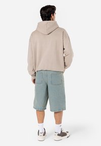 Beige hooded sweatshirt paired with light blue denim shorts. Footwear features a mix of white and gray tones. Casual, relaxed fit.