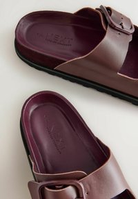 Sandales marron avec une sangle à boucle, fabriquées en matériau synthétique lisse. Semelle sombre, semelle légèrement texturée avec un marquage en relief.