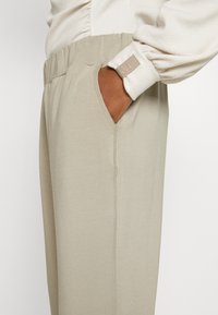 Calças de moletom bege com cintura elástica e bolso lateral, apresentando detalhes de costura visíveis. O material parece suave e leve.