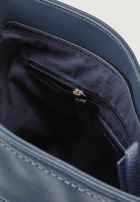 Interno della borsa in pelle blu navy con una texture liscia, dotato di una tasca con zip e dettagli cuciti lungo i bordi. Fodera in tessuto scuro.